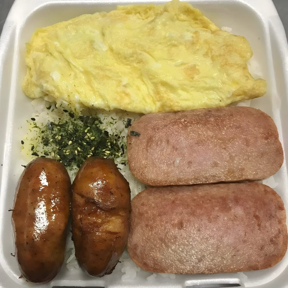 Poke Etc. plate lunch with omelet, spam, sausages, rice, and furikake in a styrofoam container.