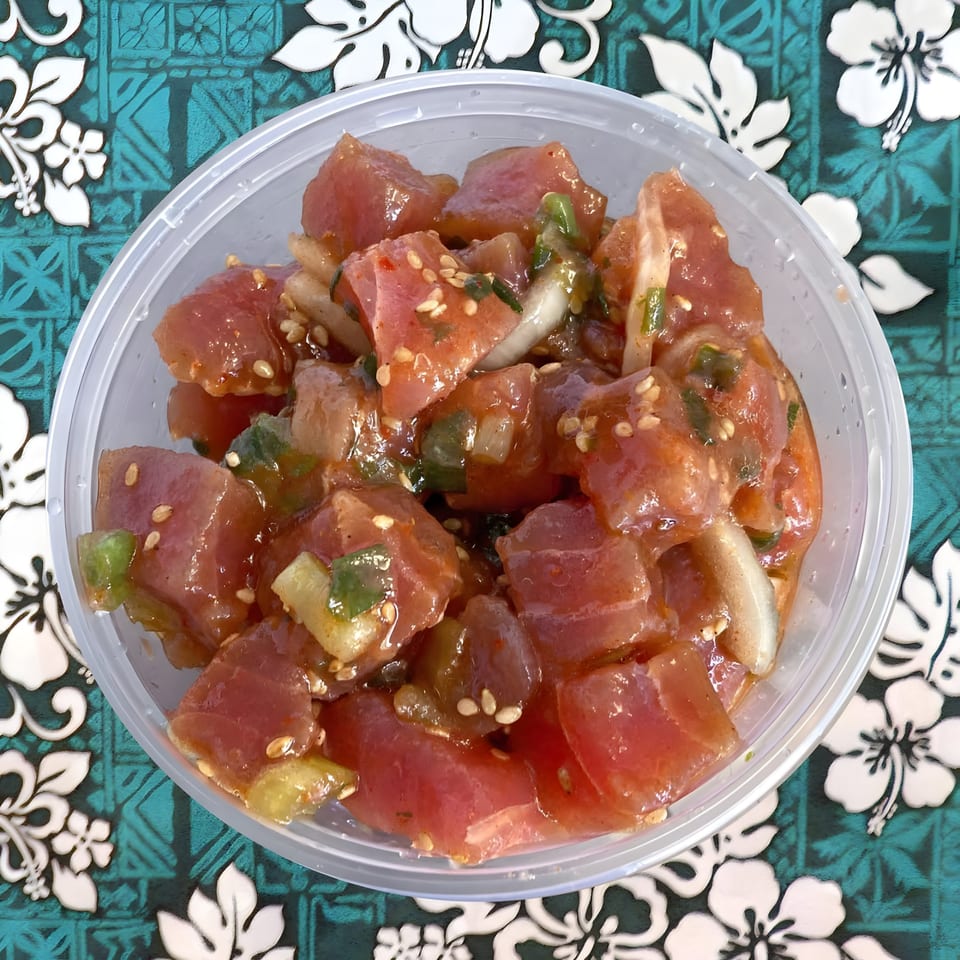A clear plastic container filled with Poke Etc's fresh poke, featuring cubed tuna, onions, and sesame seeds.